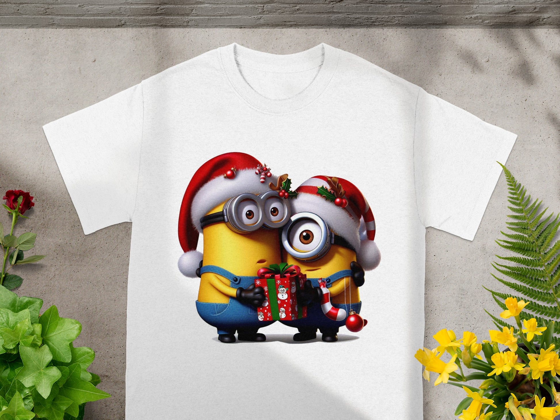 Two Minions in Santa hats hold a gift and candy cane on a white t-shirt.
