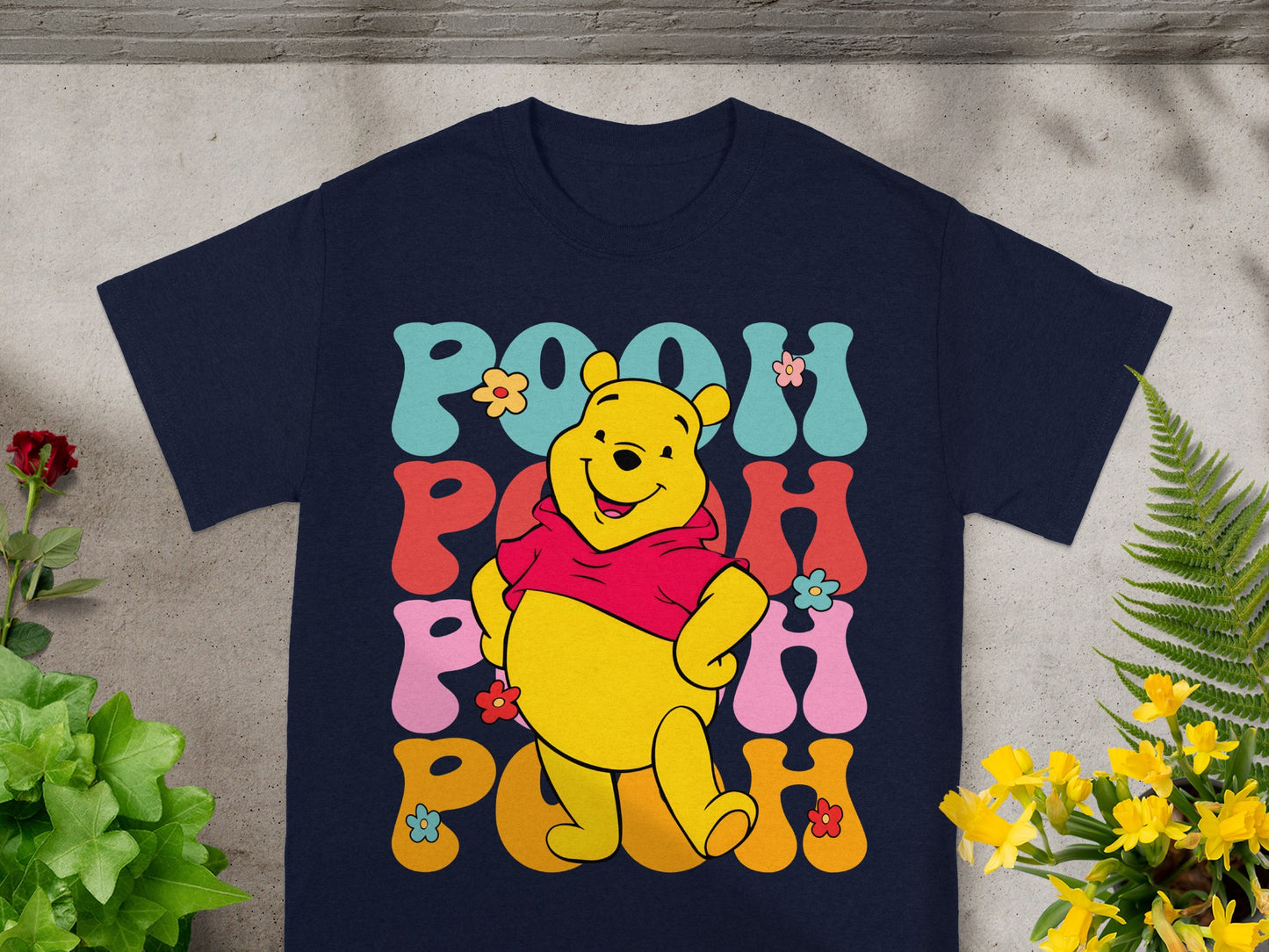 Winnie the Pooh in groovy font with flowers on a navy t-shirt.