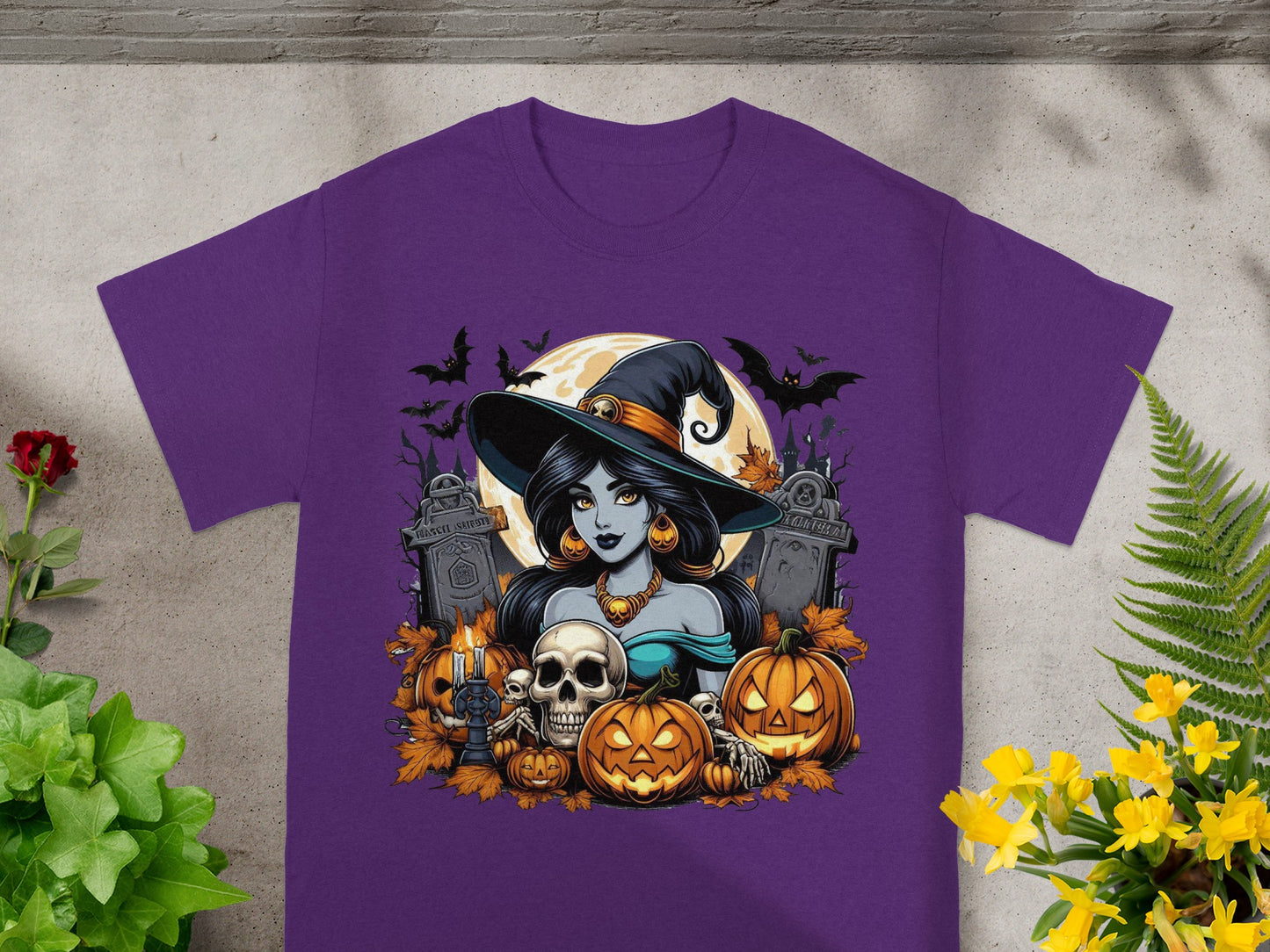Halloween graphic with a witch, pumpkins, skulls, and bats on a purple t-shirt.