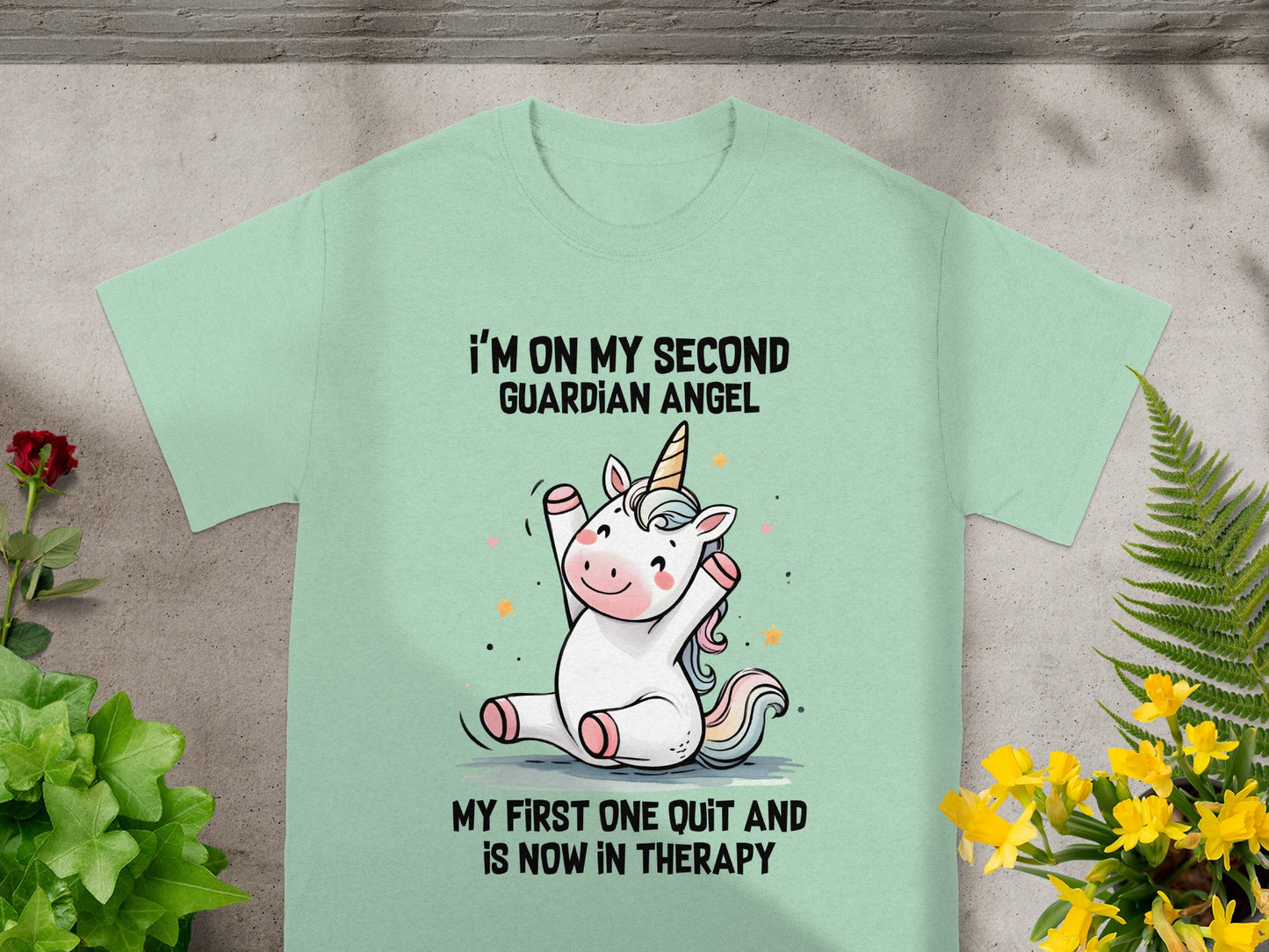 Mint t-shirt with unicorn graphic and text: "I'm on my second guardian angel. My first one quit and is now in therapy."