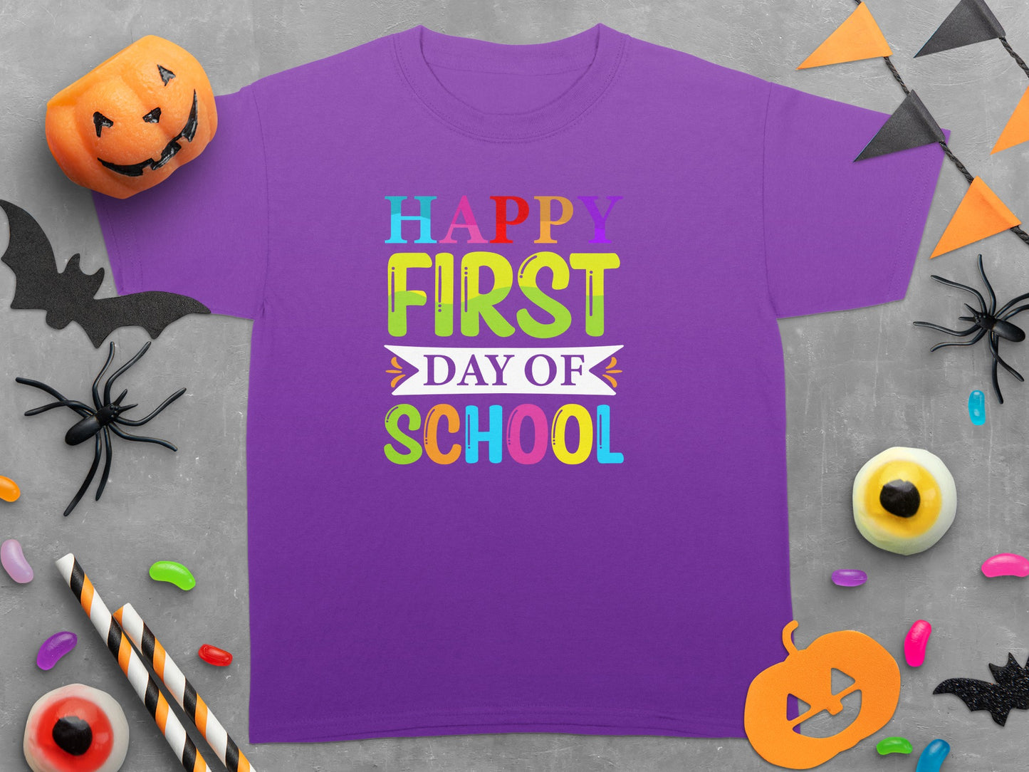 Purple t-shirt with "Happy First Day of School" text surrounded by Halloween decorations.