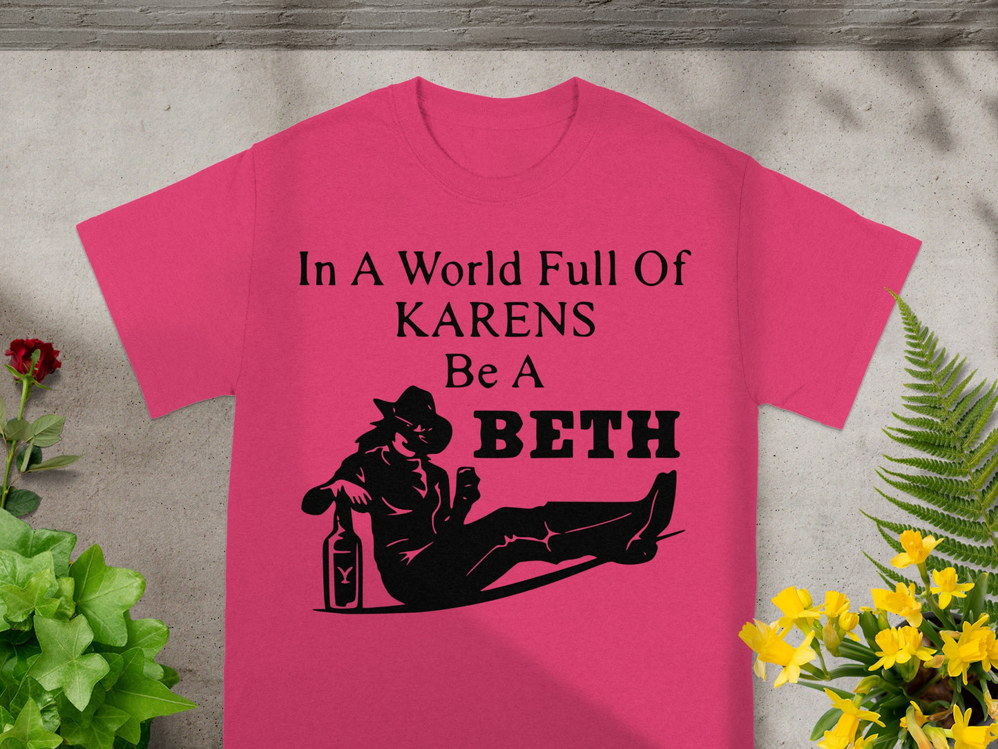 Pink t-shirt with text "In A World Full Of KARENS Be A BETH" and a reclined figure.