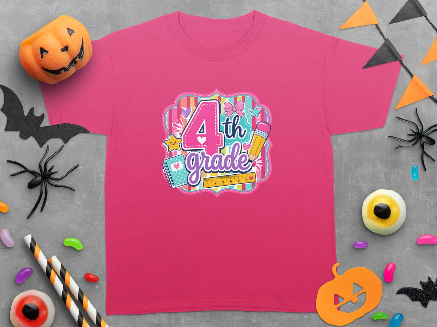 Pink t-shirt with "4th grade" text and school supplies graphic, surrounded by Halloween decorations.