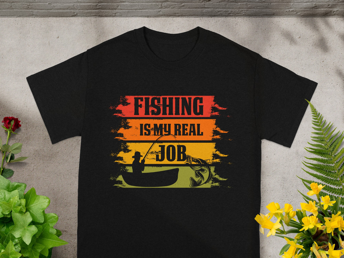 Black t-shirt with "Fishing is my real job" text, a fisherman in a boat, and a fish.