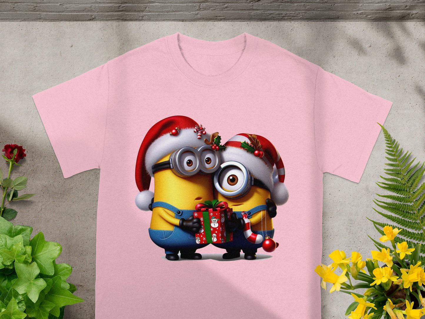Two Minions wearing Santa hats, one holding a gift and candy cane, on a pink t-shirt.