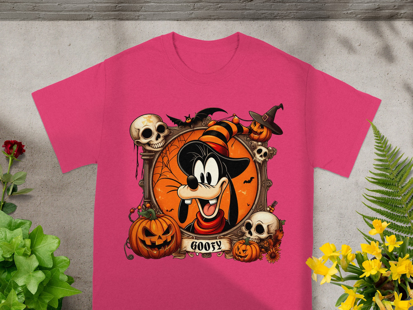 Goofy Halloween graphic with pumpkins, skulls, and bats on a pink t-shirt.