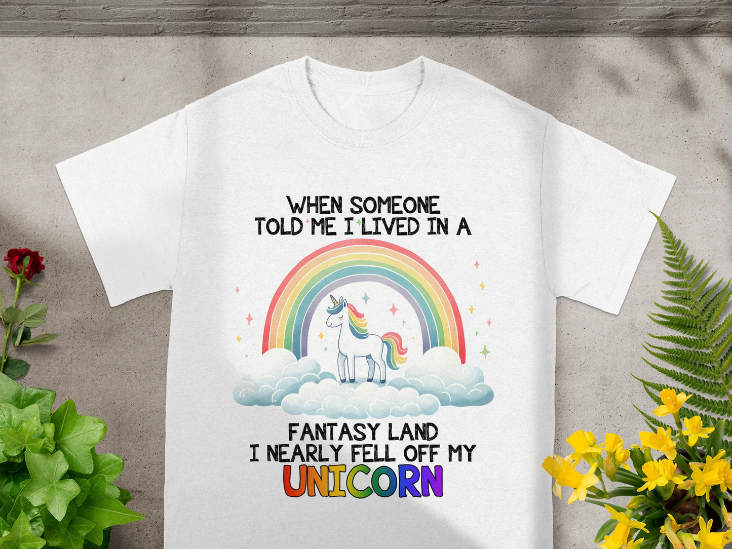 White t-shirt with unicorn, rainbow, clouds, and text: "When someone told me I lived in a fantasy land I nearly fell off my Unicorn."