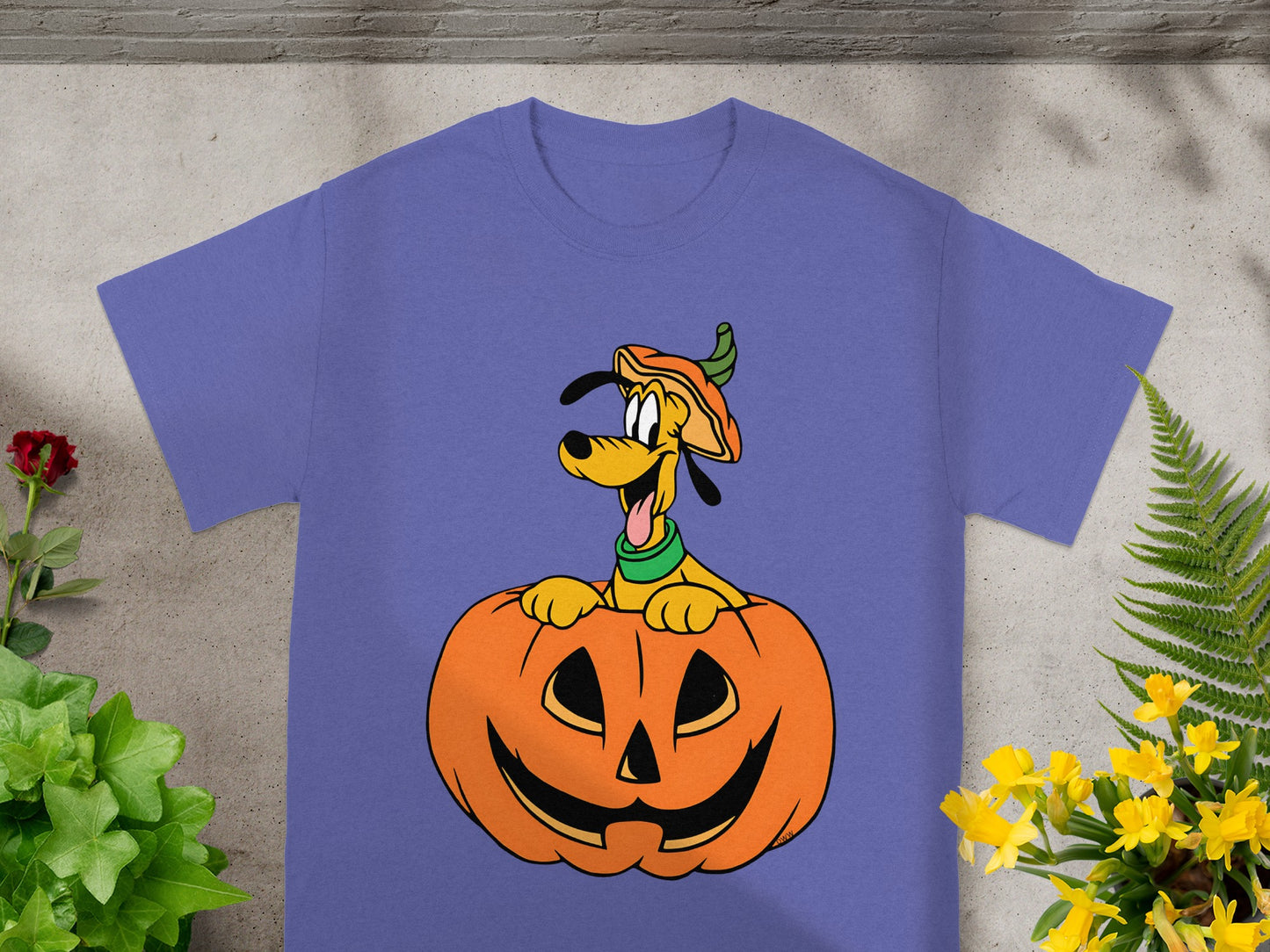 Pluto wearing a pumpkin hat peeks out of a carved jack-o'-lantern on a purple t-shirt.