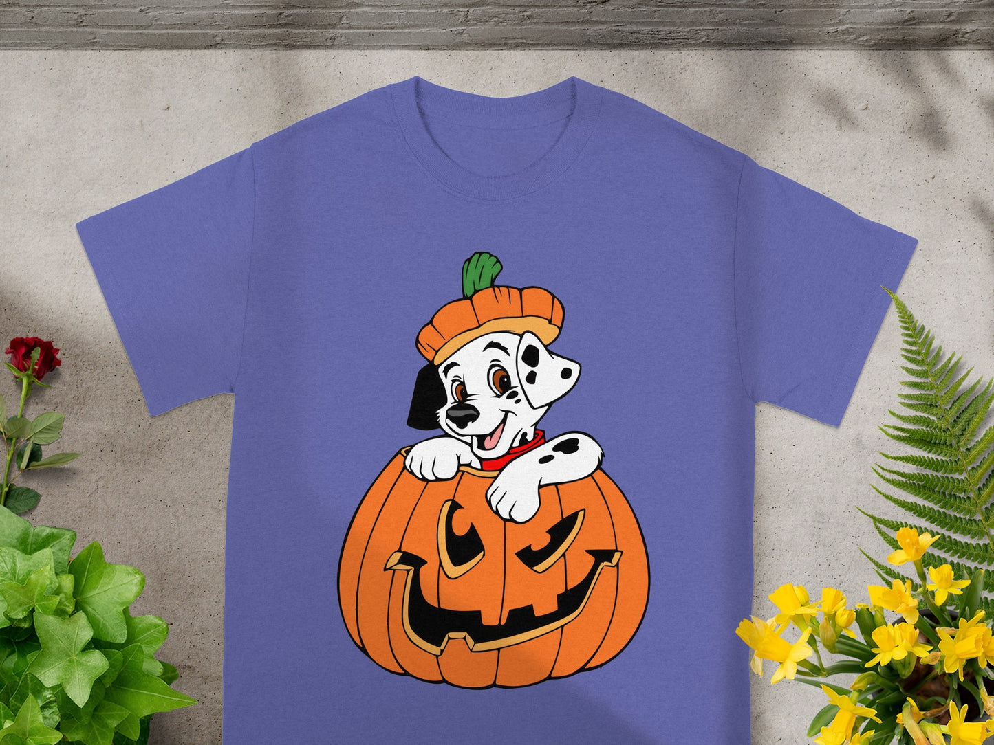 Dalmatian puppy wearing pumpkin hat peeking out of jack-o'-lantern on purple t-shirt.