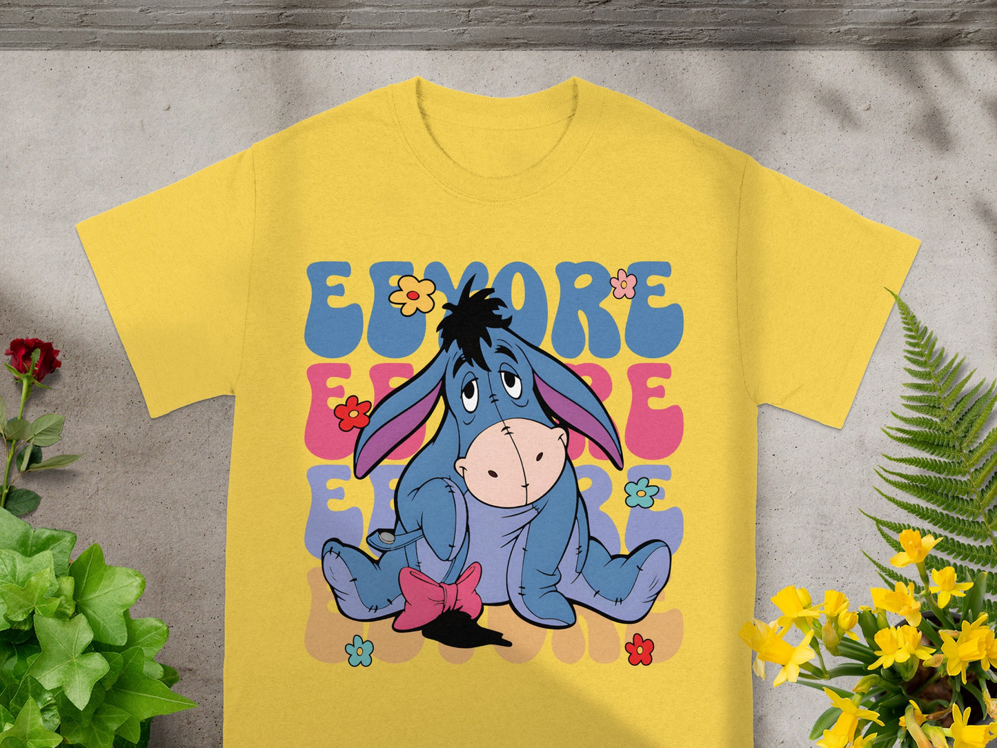 Eeyore from Winnie the Pooh on a yellow t-shirt with colorful text and flowers.