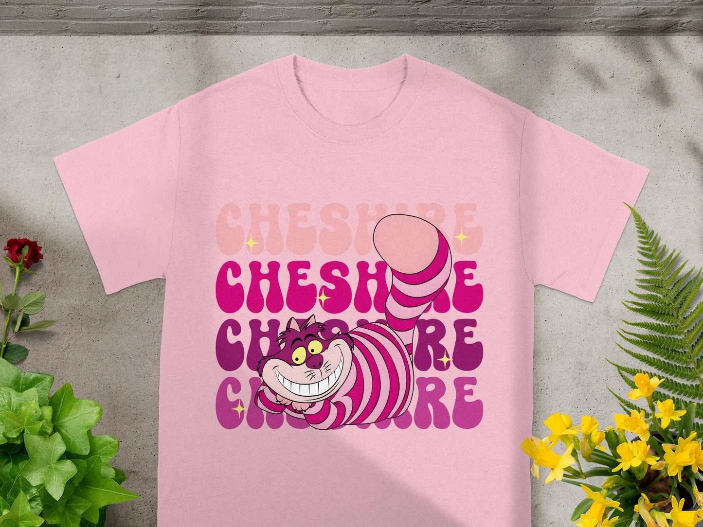Pink t-shirt with purple Cheshire Cat graphic and text.