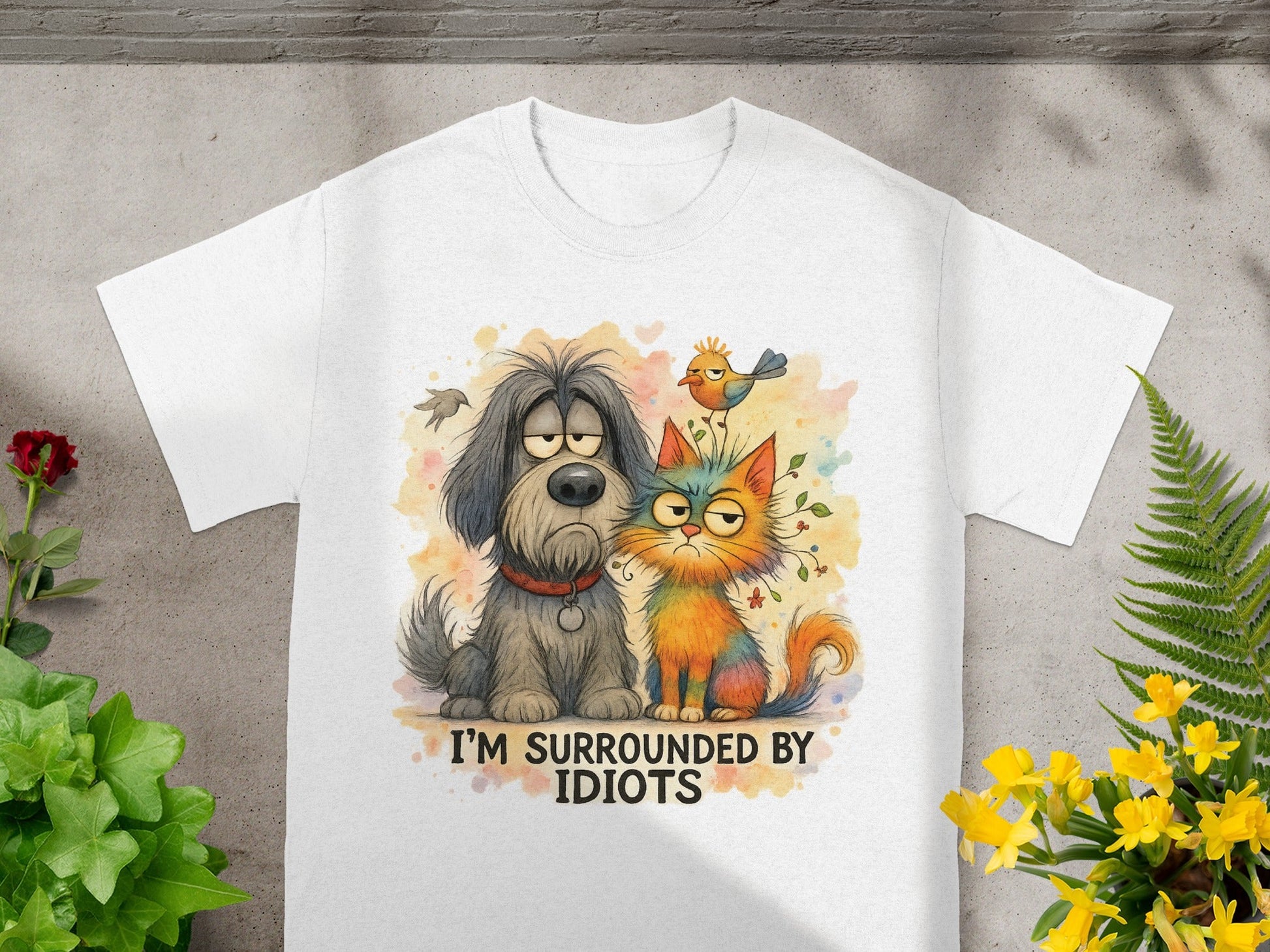 White t-shirt with watercolor illustration of a sad dog and a grumpy cat with the text "I'M SURROUNDED BY IDIOTS".