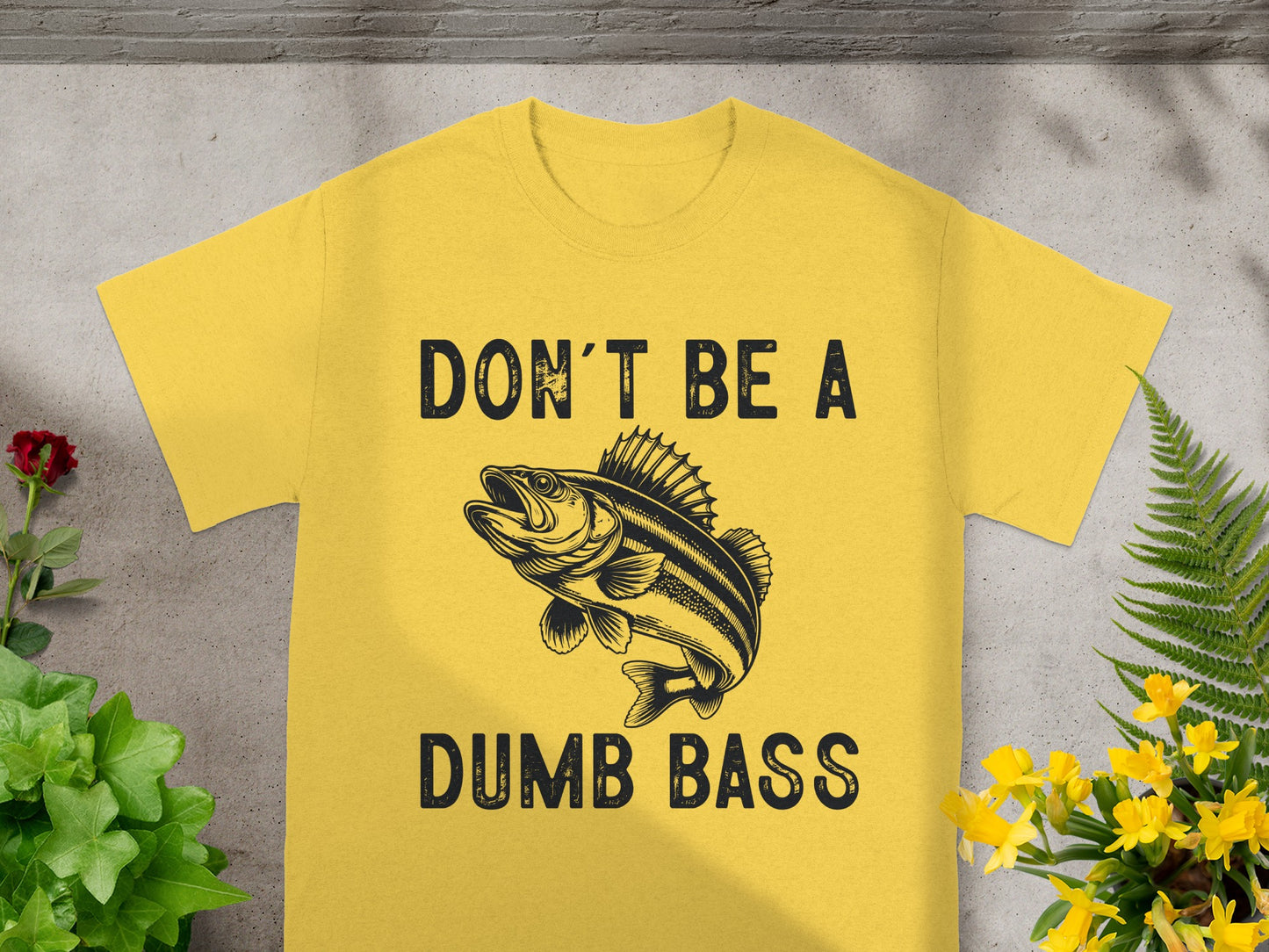 Yellow t-shirt with black text "DON'T BE A" above a bass fish graphic and "DUMB BASS" below.