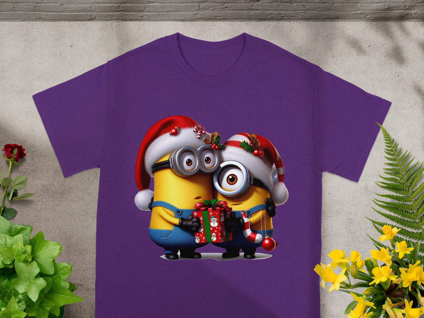 Two Minions in Santa hats hug a Christmas gift and candy cane on a purple shirt.