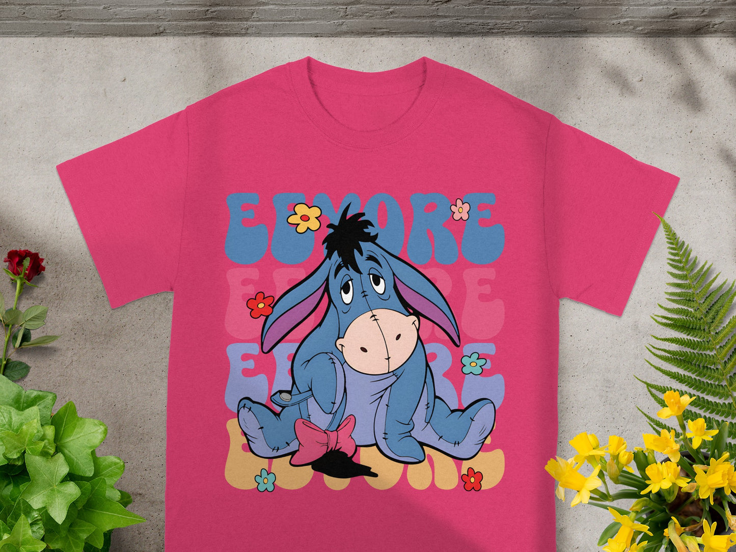 Eeyore character with flowers on a pink t-shirt, "EEYORE" text design.
