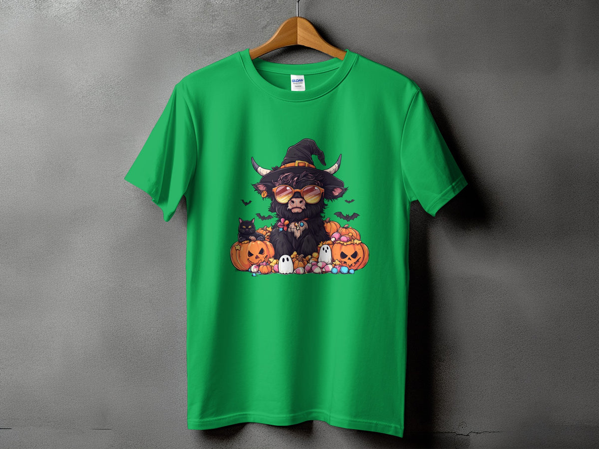 Green t-shirt with a cartoon highland cow wearing a witch hat and sunglasses, surrounded by pumpkins and ghosts.