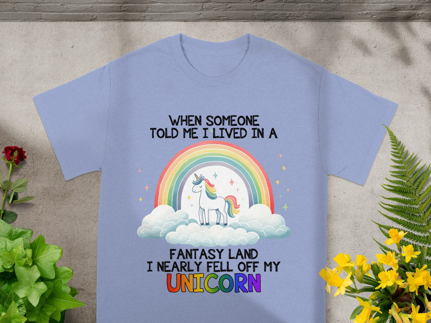 Light purple shirt with unicorn, rainbow, clouds, and text: "When someone told me I lived in a fantasy land I nearly fell off my unicorn".