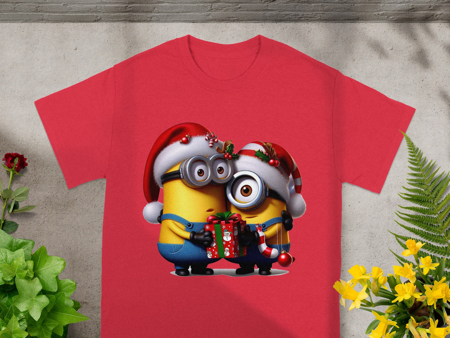 Two Minions wear Santa hats, holding a gift and candy cane on a red t-shirt.