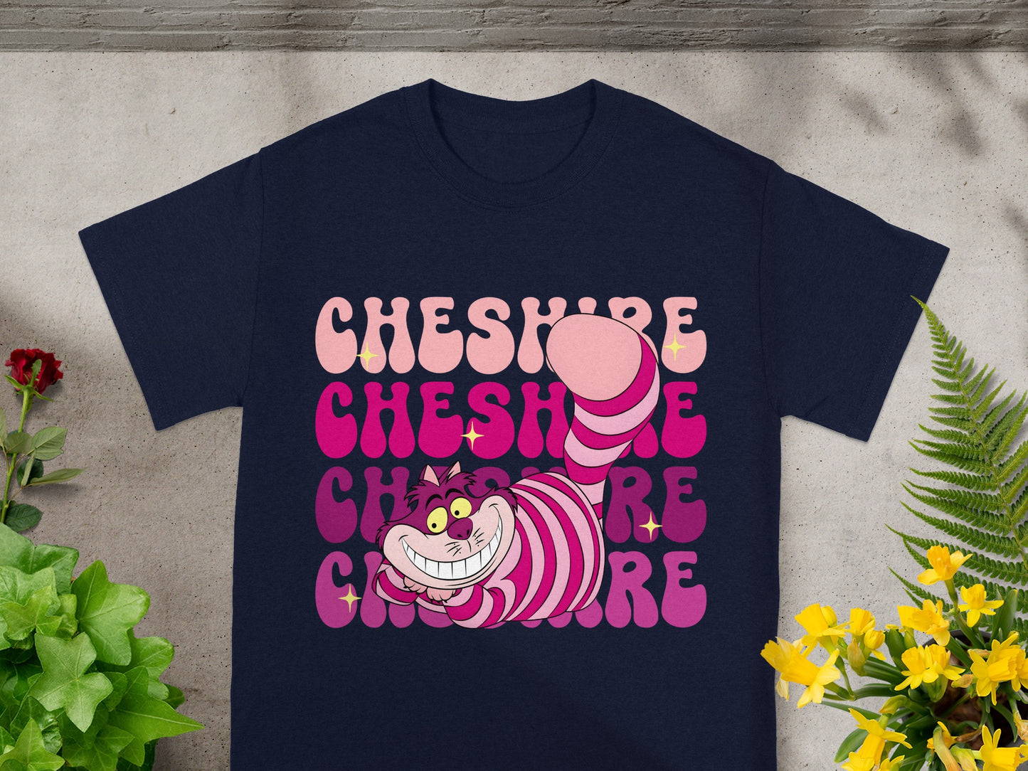 Cheshire Cat smiling with "Cheshire" text in pastel gradient on navy t-shirt.
