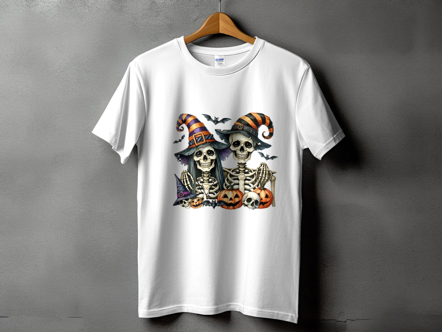 Two skeletons in witch hats with pumpkins and bats on a white t-shirt.