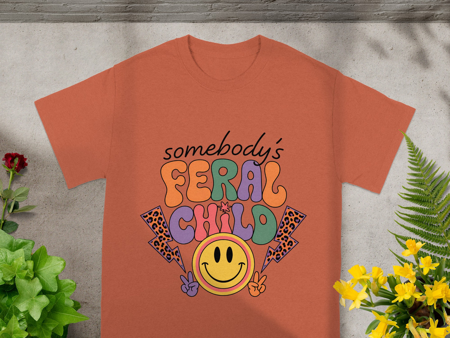 Orange t-shirt with "somebody's FERAL CHILD" text and smiley face graphic.