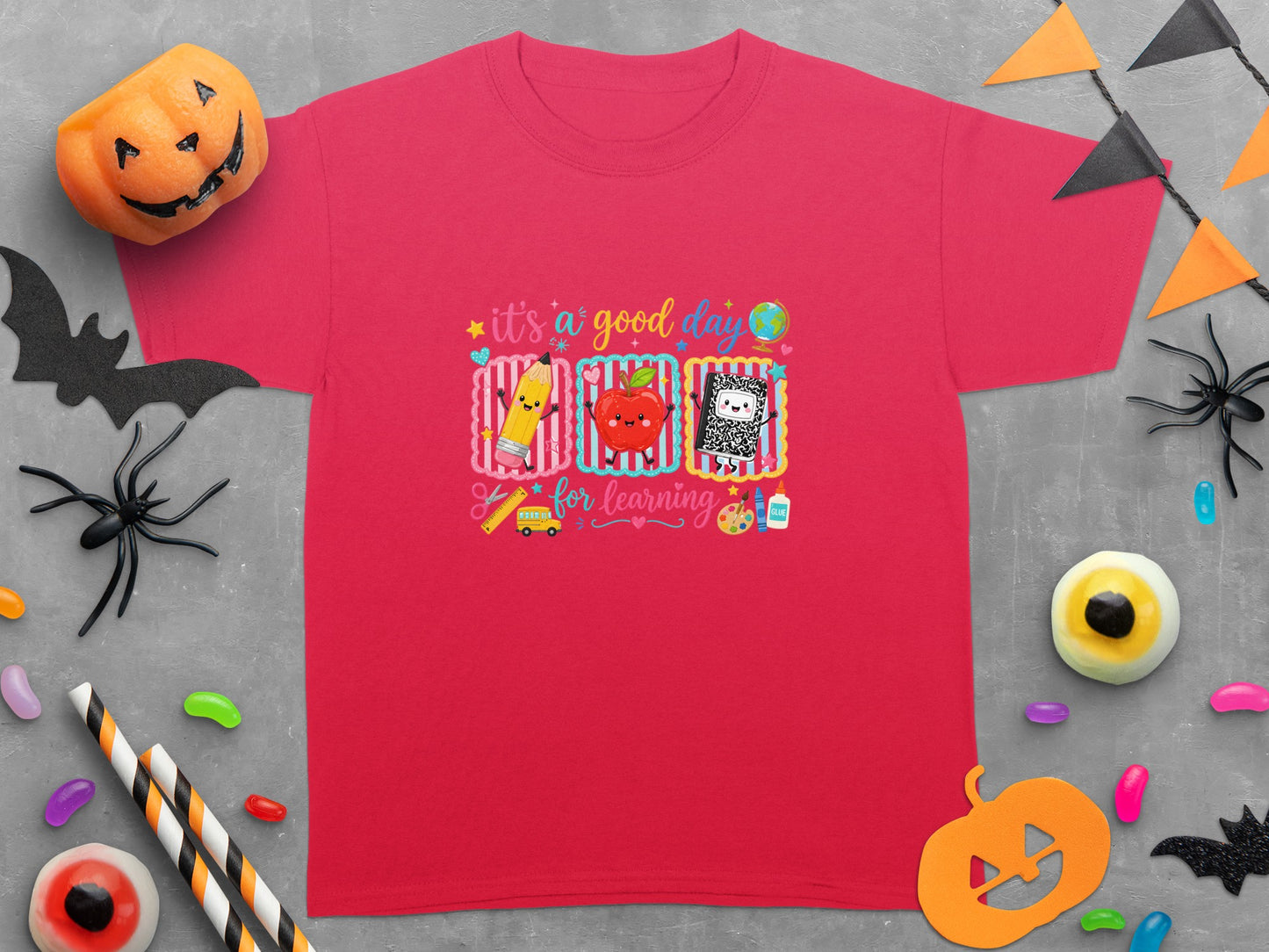 Red t-shirt with "it's a good day for learning" graphic, featuring cartoon school supplies and Halloween decorations.