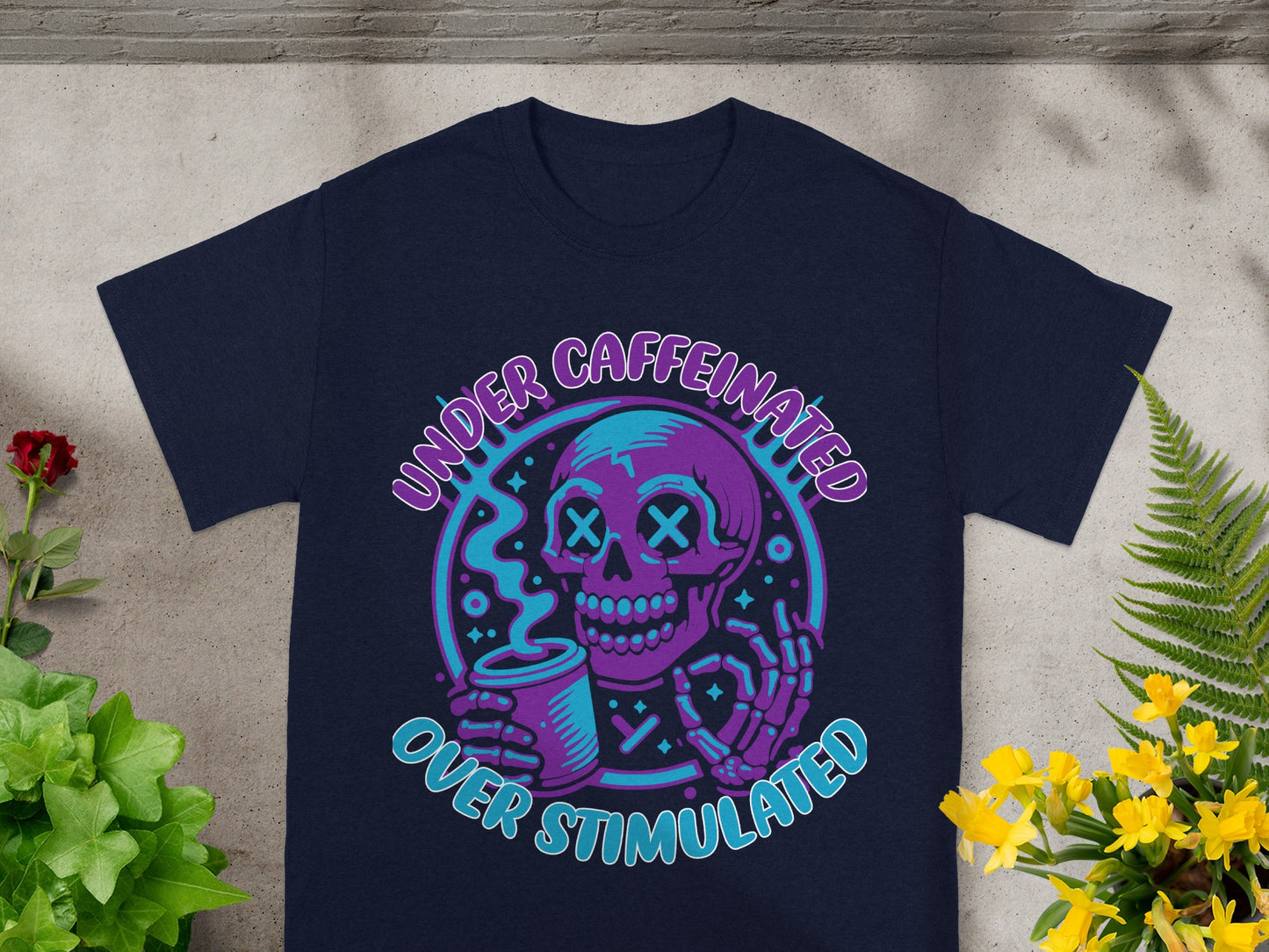 Skull holding coffee cup graphic with text "Under Caffeinated Over Stimulated".
