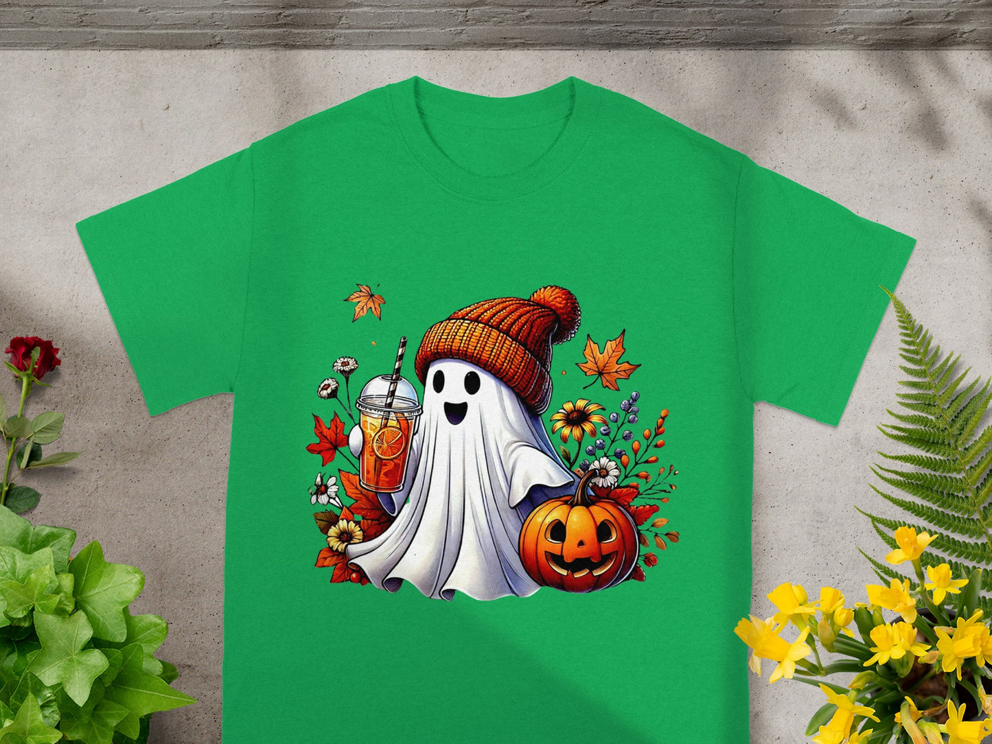 Green t-shirt with cartoon ghost holding drink and pumpkin, surrounded by leaves.