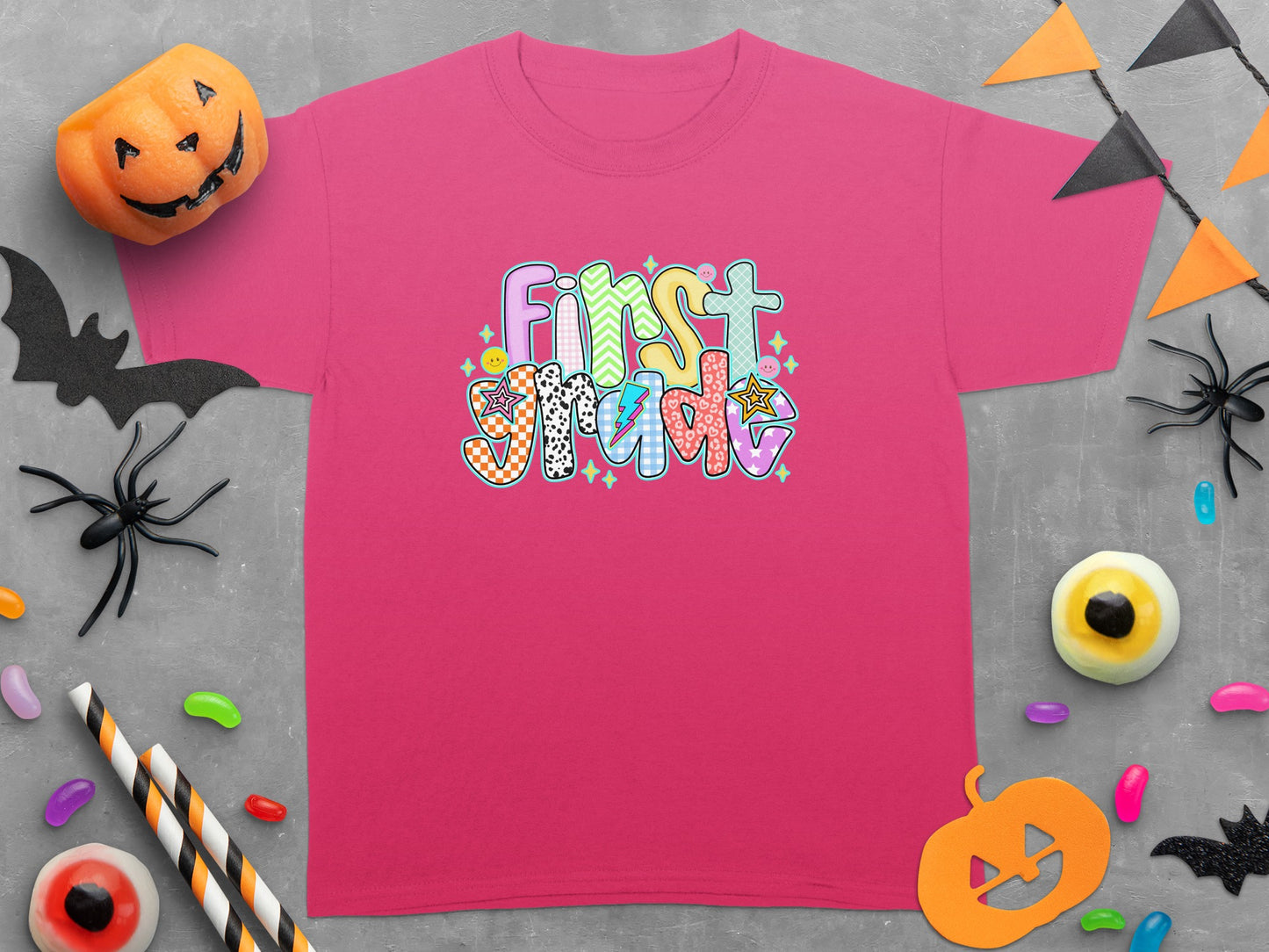Pink t-shirt with "First Grade" text in colorful, patterned letters.