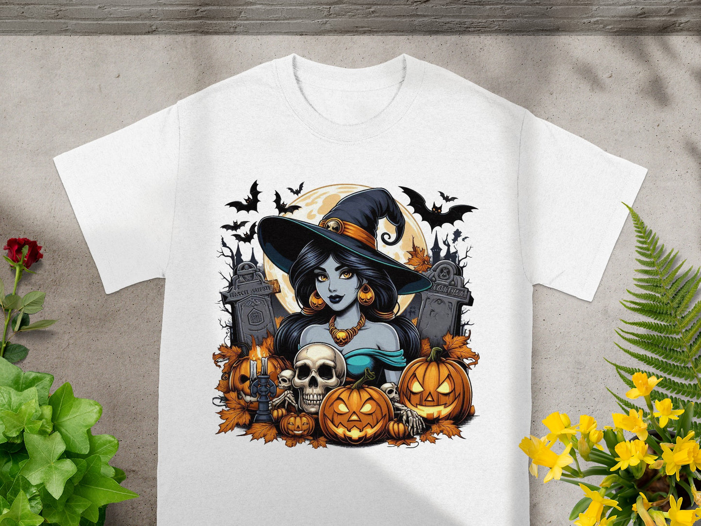 Halloween witch illustration with pumpkins, skulls, bats, and gravestones on a white t-shirt.