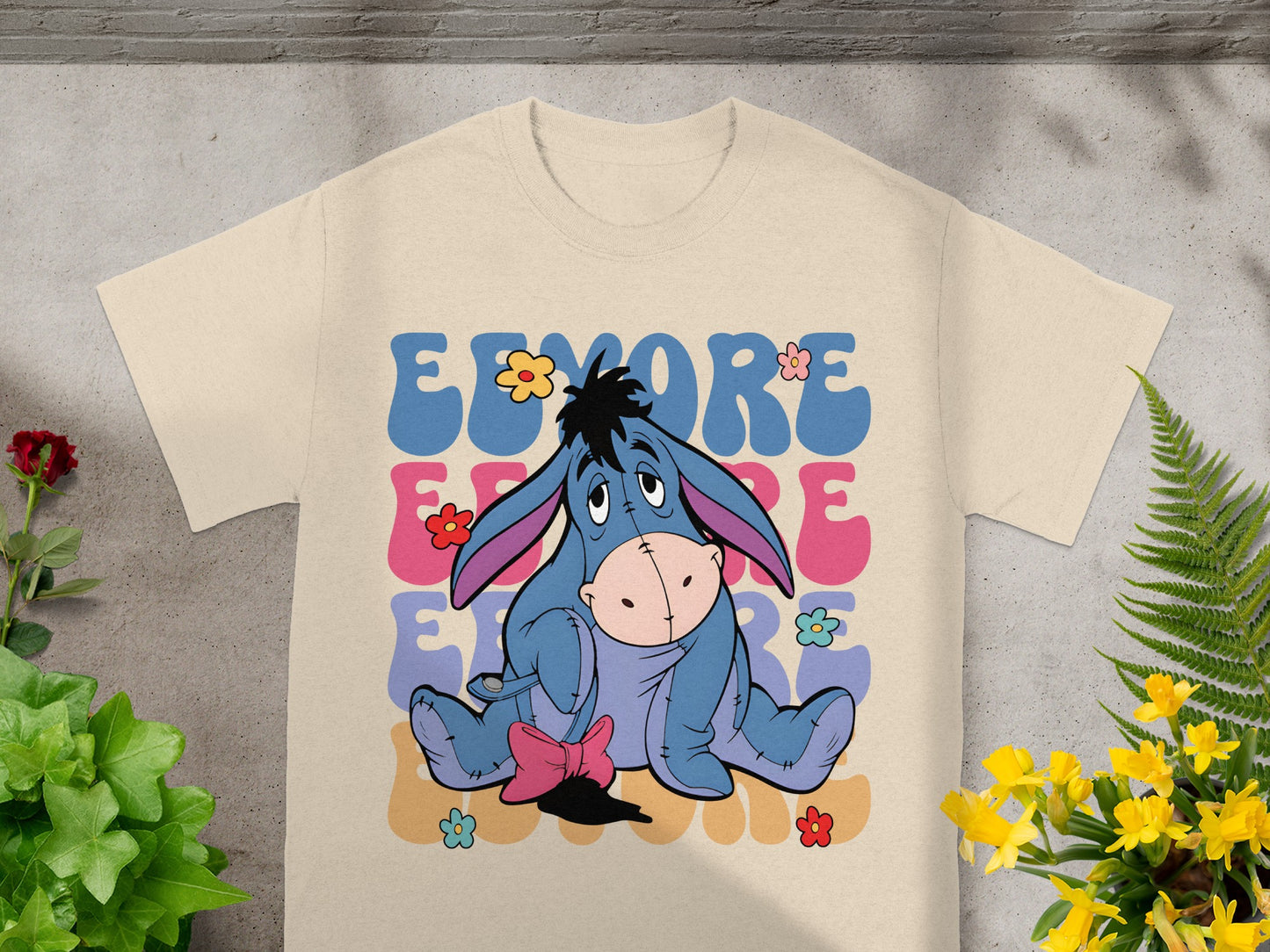 Eeyore with flowers graphic on a beige t-shirt.