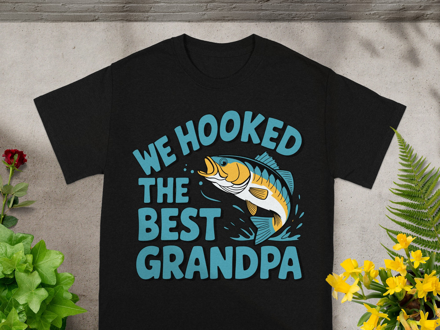 Black t-shirt with "We Hooked The Best Grandpa" text and a jumping fish graphic.