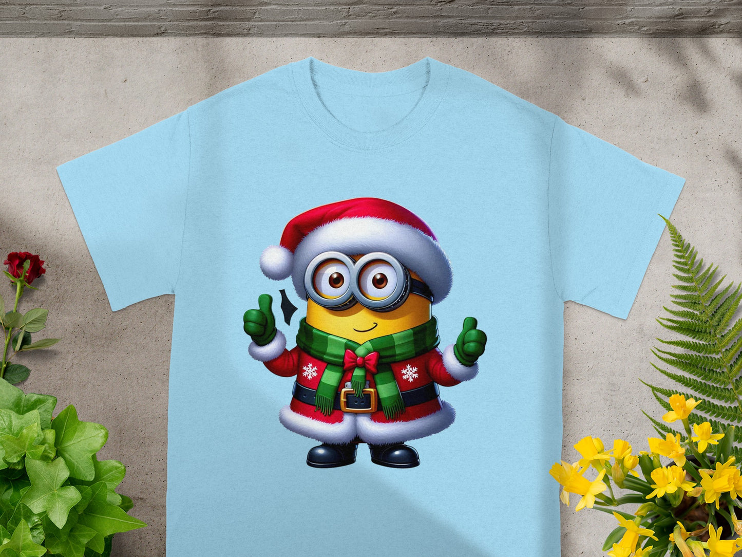 Minion in Santa costume with green scarf giving thumbs up on light blue t-shirt.