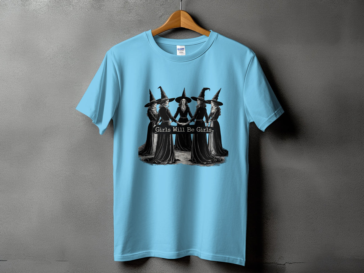 Light blue t-shirt featuring a graphic of five women in witch hats and text "Girls Will Be Girls."