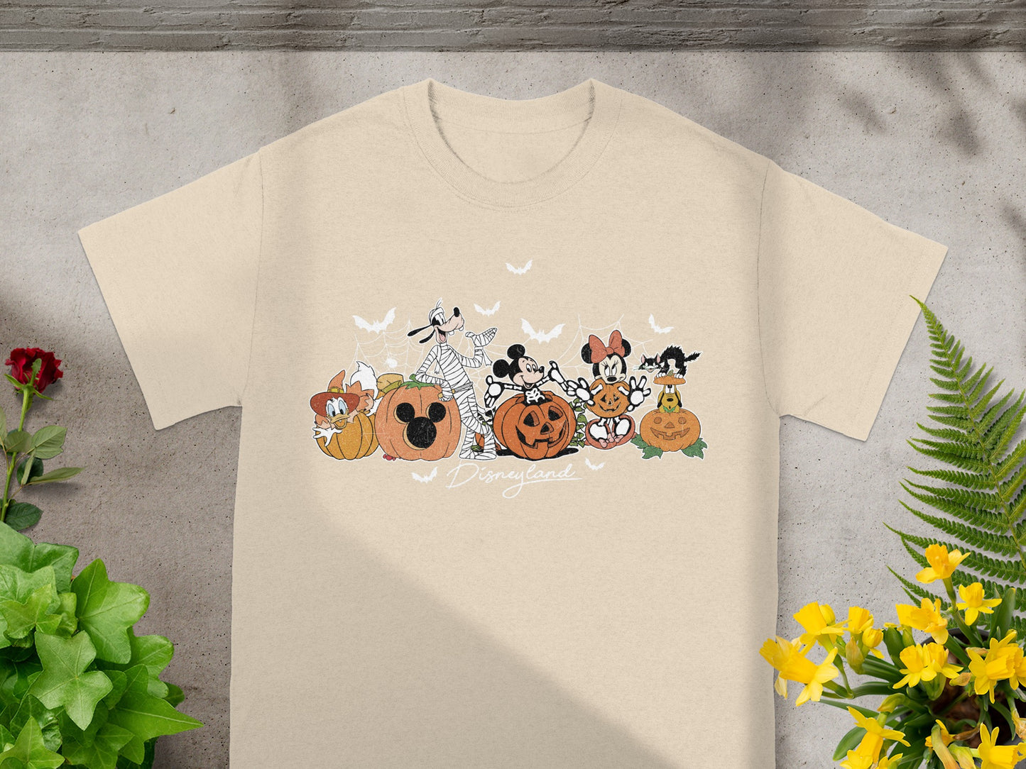 Disneyland characters and pumpkins graphic with text on a light tan t-shirt.