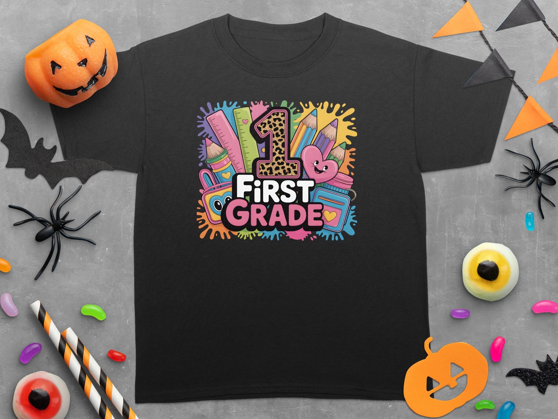 Black t-shirt with "First Grade" text surrounded by colorful school supplies and playful graphics.