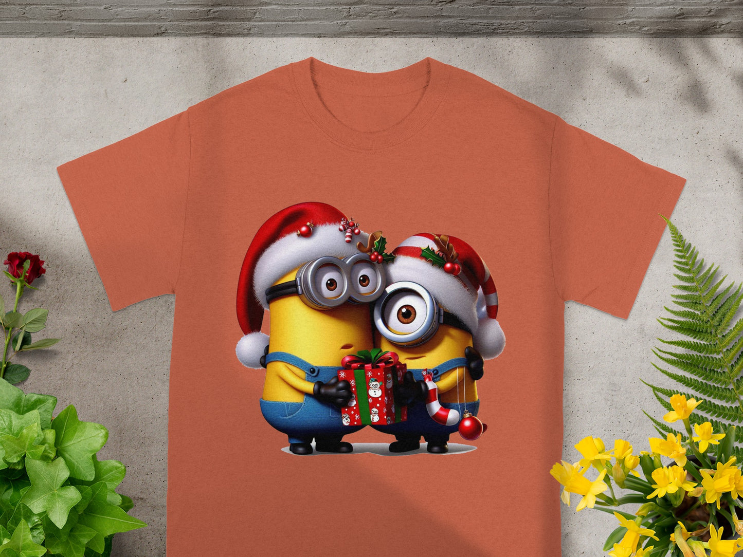 Two Minions in Santa hats holding a gift and candy cane on an orange t-shirt.