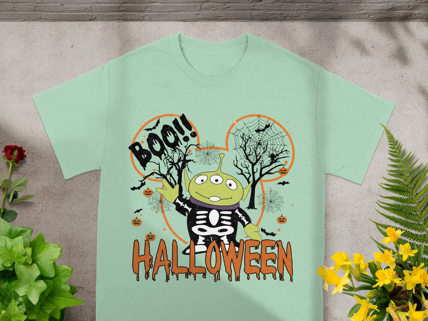 Alien character in skeleton costume on light green t-shirt with "Boo!!" and "Halloween" text.