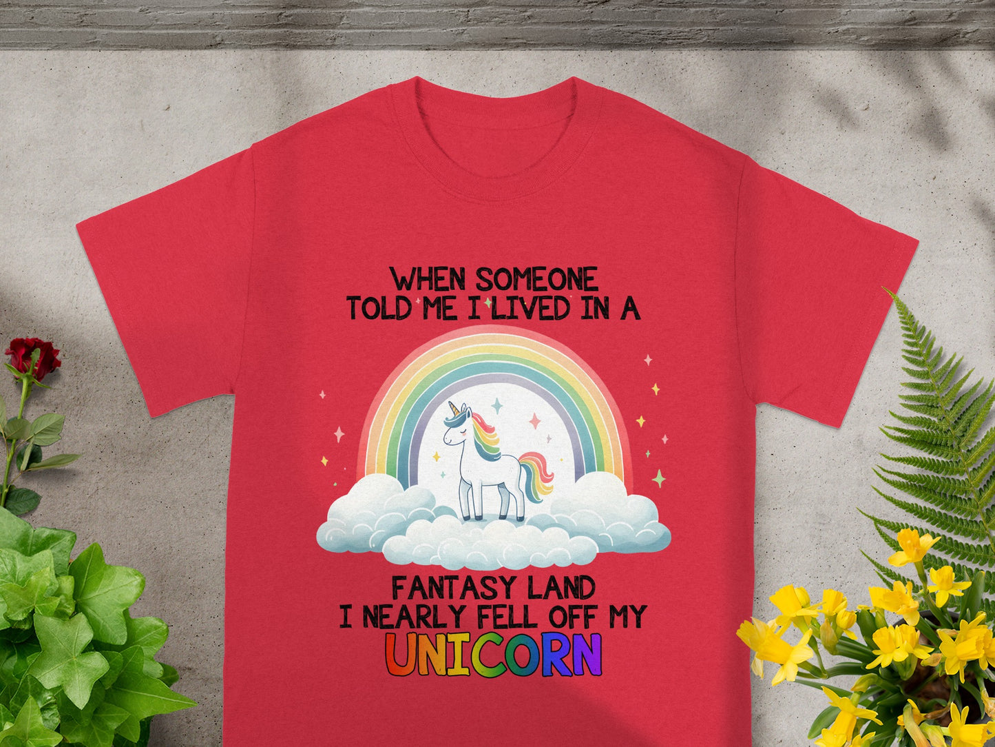 Red t-shirt with a unicorn, rainbow, and text about living in a fantasy land.