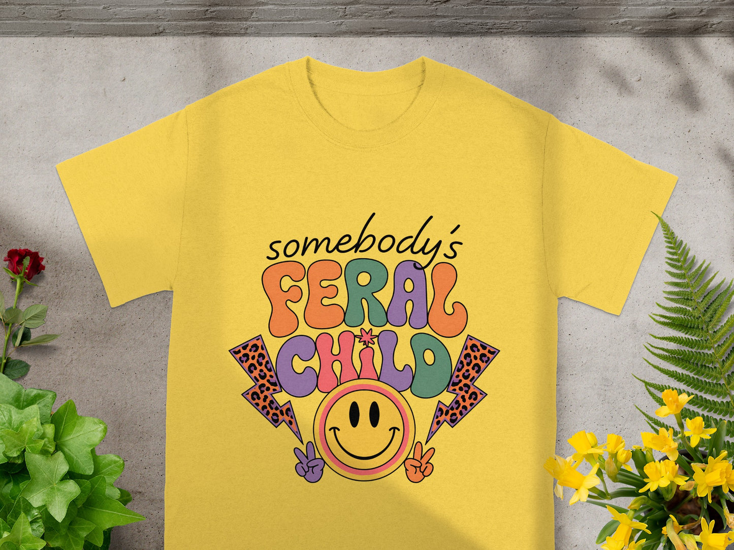 Yellow t-shirt with "somebody's FERAL CHILD" text, smiley face, and lightning bolts.