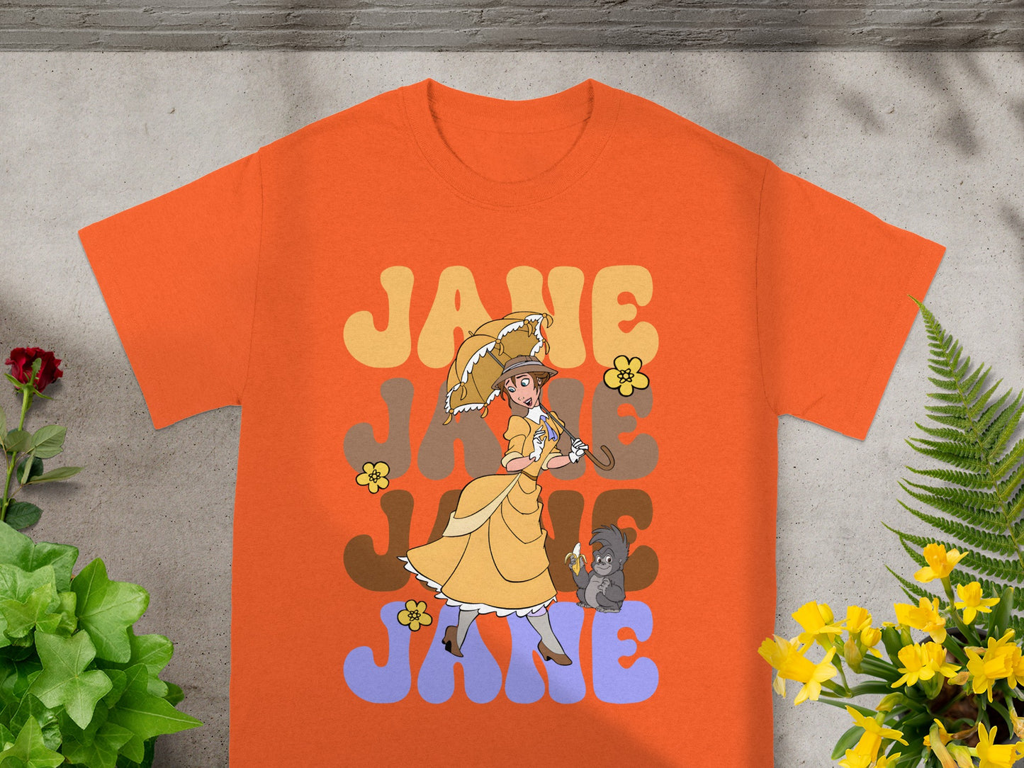 Orange t-shirt graphic with "Jane" in large groovy font and a woman with a parasol.