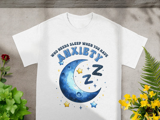 White t-shirt with blue text "WHO NEEDS SLEEP WHEN YOU HAVE ANXIETY" and crescent moon graphic.