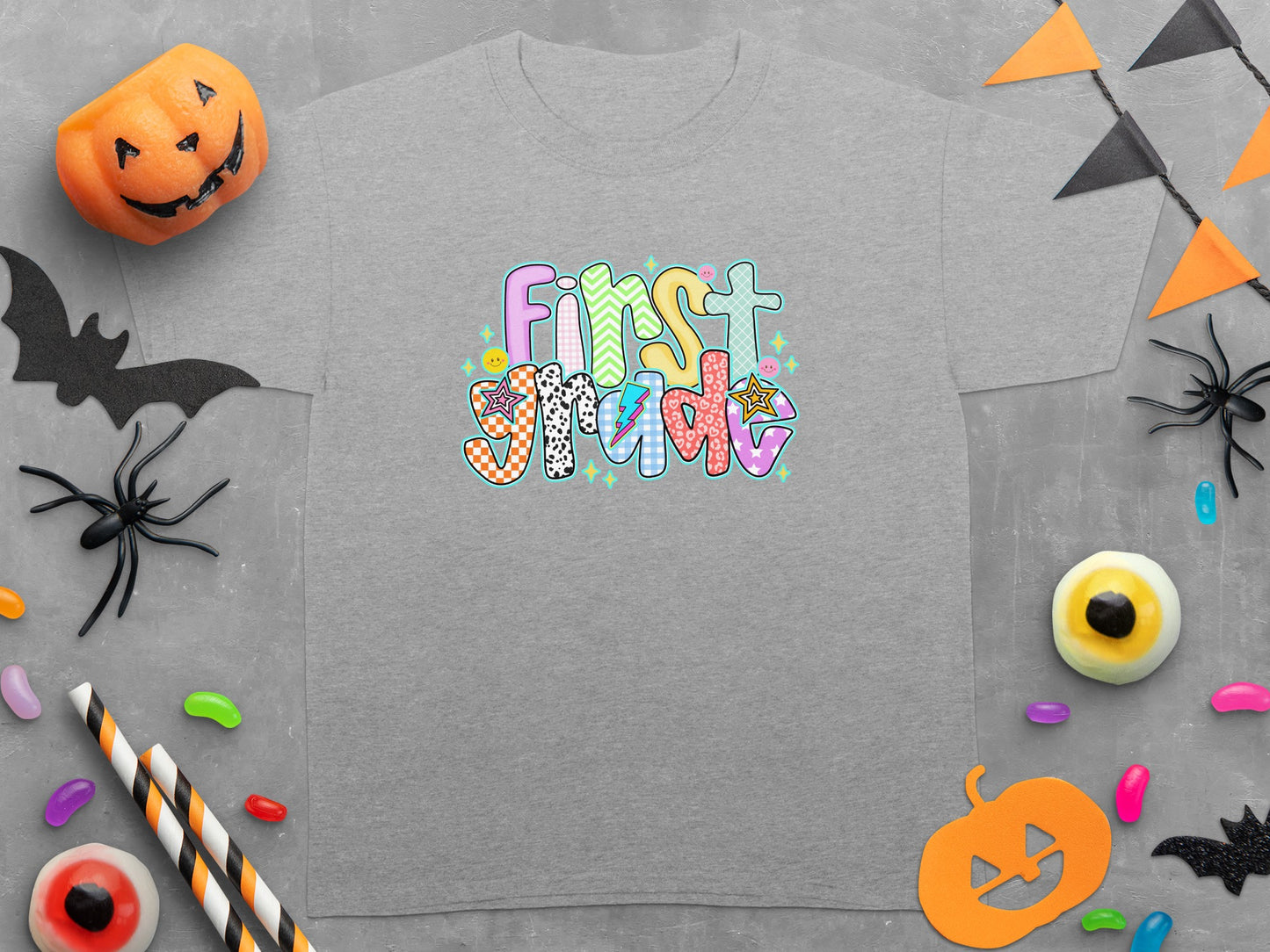 Grey t-shirt with colorful "First Grade" text and Halloween decorations.
