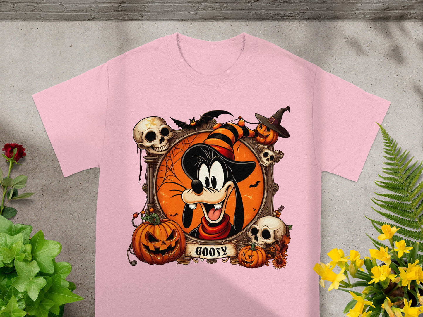 Goofy Halloween graphic with pumpkins, skulls, bats, and text on a pink t-shirt.