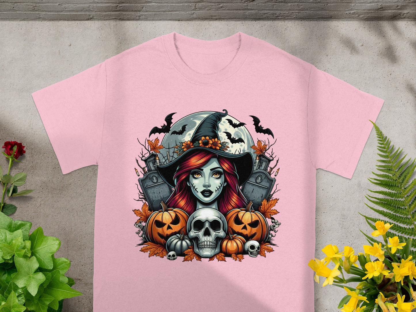 Pink t-shirt featuring a Halloween graphic with a witch, pumpkins, skulls, and bats.