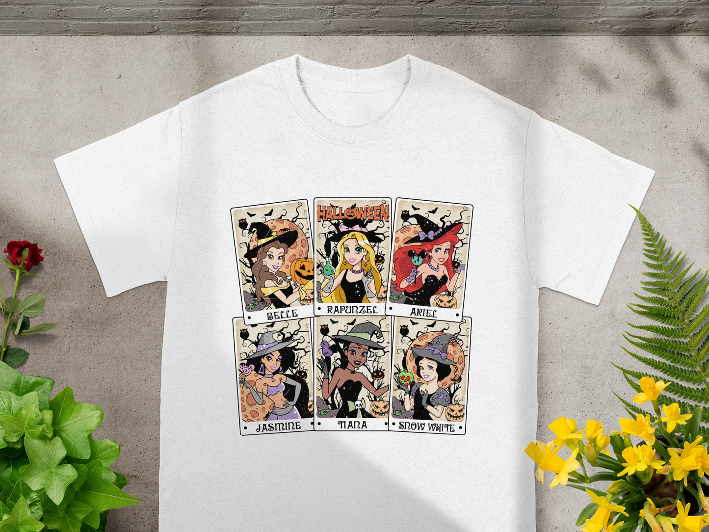 White t-shirt featuring six Halloween-themed Disney princess tarot cards: Belle, Rapunzel, Ariel, Jasmine, Tiana, Snow White.