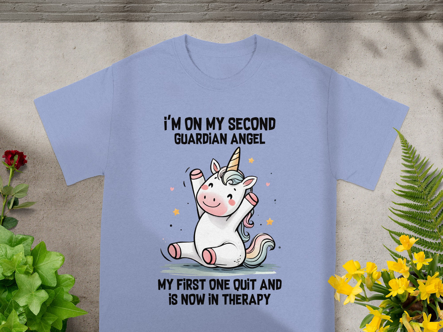 Light purple t-shirt with a cartoon unicorn and text: "I'M ON MY SECOND GUARDIAN ANGEL MY FIRST ONE QUIT AND IS NOW IN THERAPY."