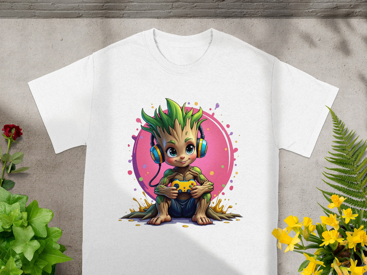 Groot wearing headphones holds a video game controller, sitting on a white t-shirt.