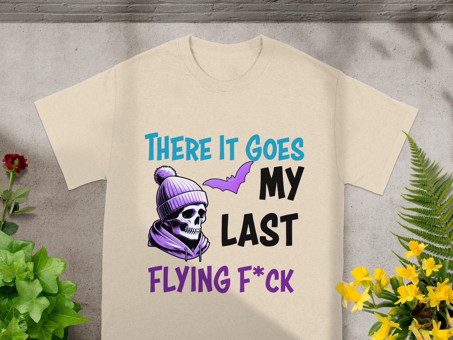 Cream t-shirt with a purple skull in a beanie, bat, and text "THERE IT GOES MY LAST FLYING F*CK".