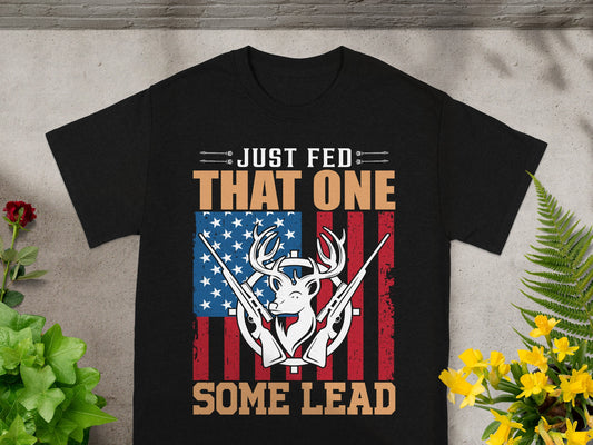 Black t-shirt with deer, guns, and American flag graphic, reading "Just Fed That One Some Lead".